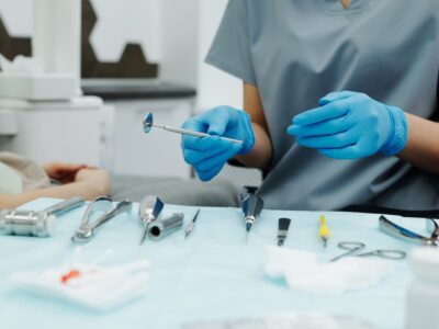 Gloved dental professional holding a dental mirror over a tray of cleaning instruments