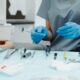 Gloved dental professional holding a dental mirror over a tray of cleaning instruments