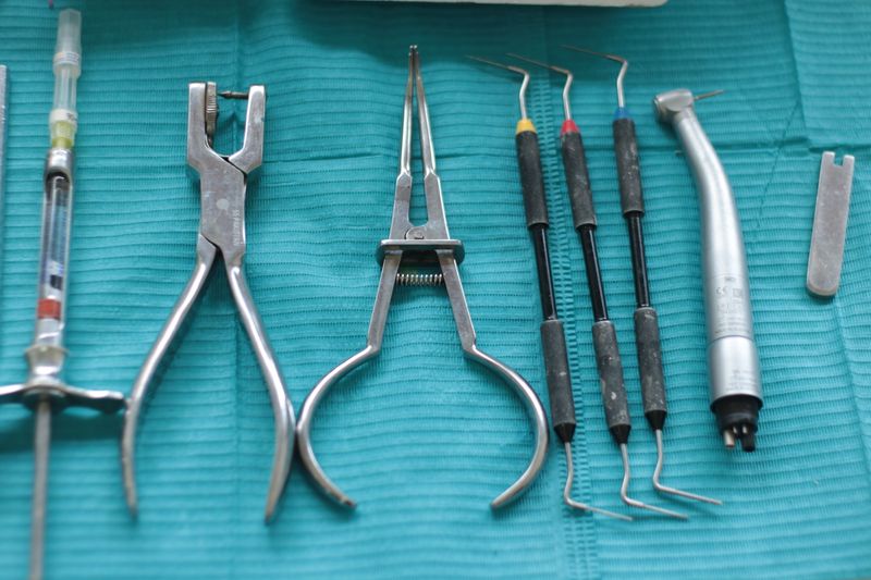 Dental anesthetic syringe, two pairs of pliers and three hand scalers laid out on a teal cloth