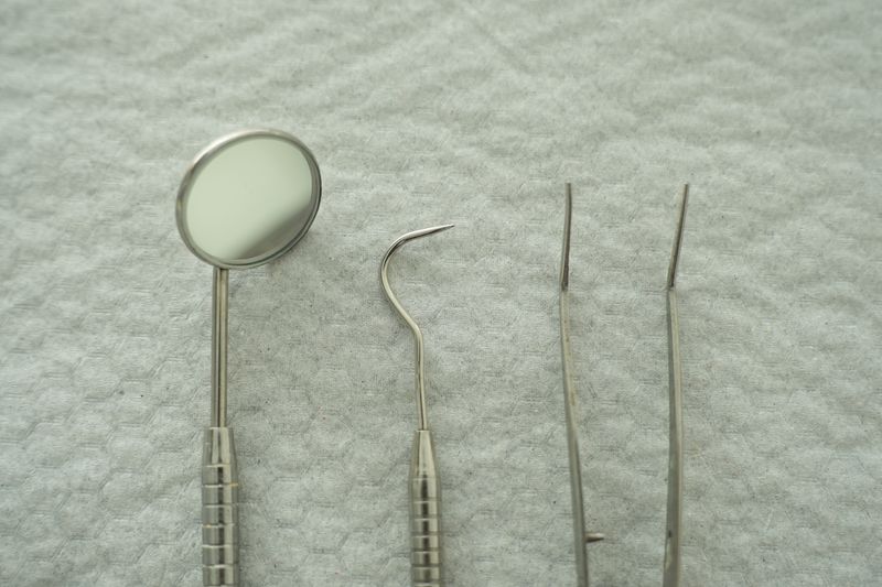 Dental mirror, explorer and two pointed hand instruments laid on a white textured cloth