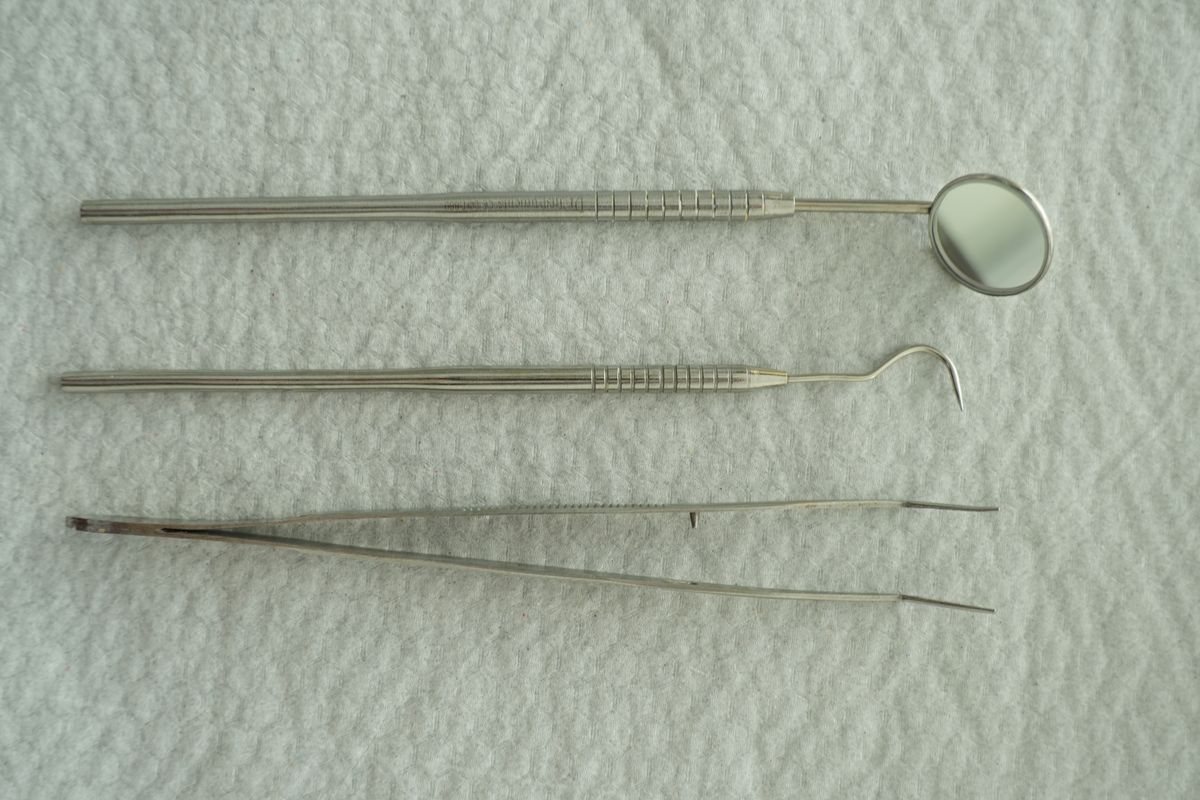 Dental exam mirror, explorer and tweezers laid on a white cloth